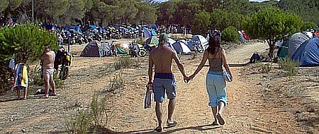 2 people surrounded by tents and bikes hold hands and walk in the glorious sunshine